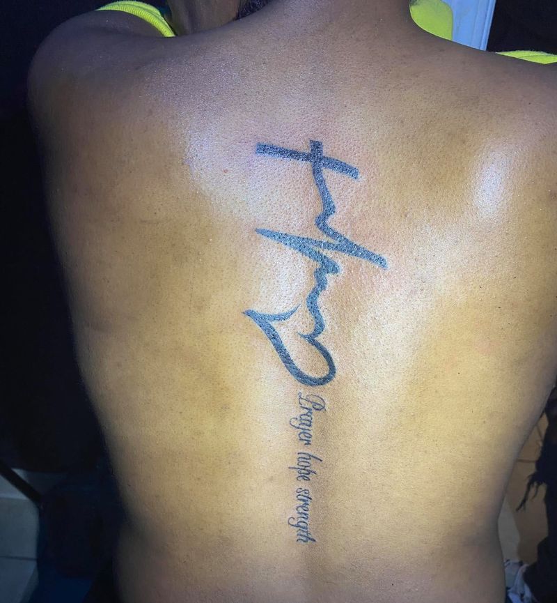 Tattoo of a cross joined to a heartbeat line and heart, with script running down the spine.
