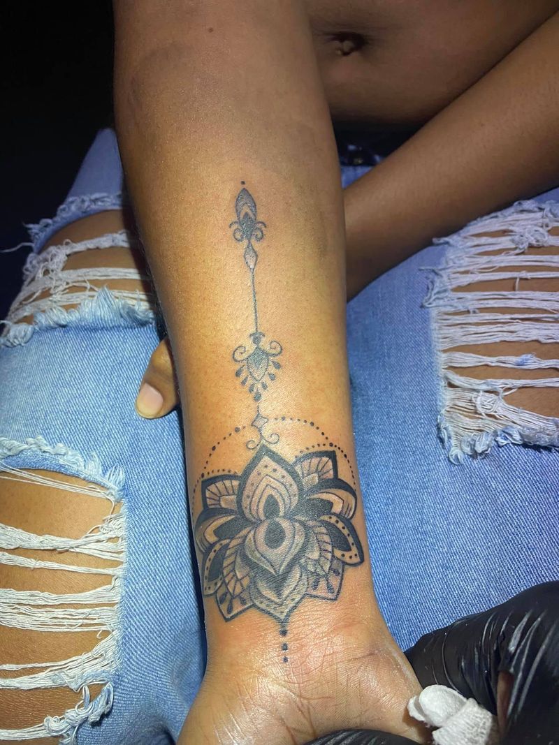 Fine black ornamental tattoo of a lotus mandala with dotwork and a decorative line running up the forearm.