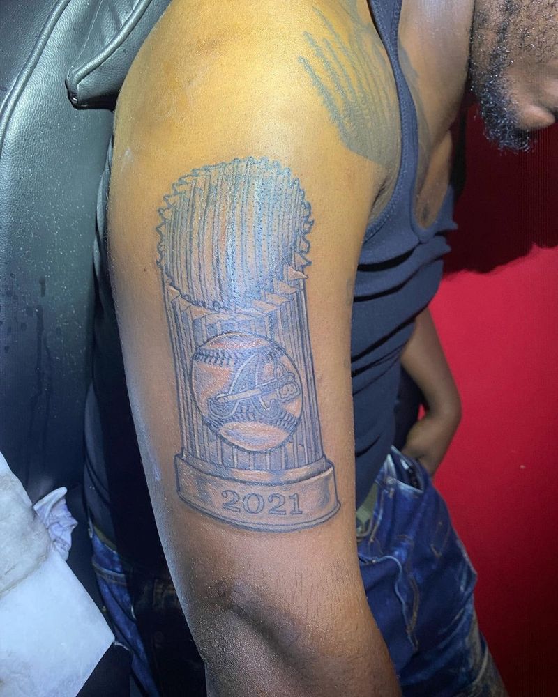 Black and grey tattoo of a trophy with the year 2021 on its base, on an upper arm.